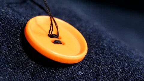 Sewing an orange button on dark jeans, denim, with black thread, close up 