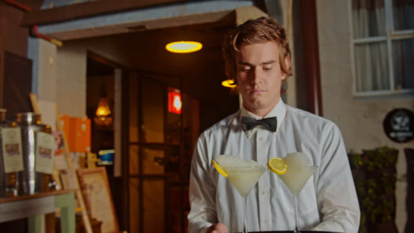 Waiter and a frozen margarita cocktail on a tray at night. Steadicam shot. 