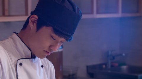 Look at this rice. Tracking shot of smiling Asian chef in white uniform standing in kitchen of sushi bar washing rice in big wooden bowl preparing it for sushi rolls