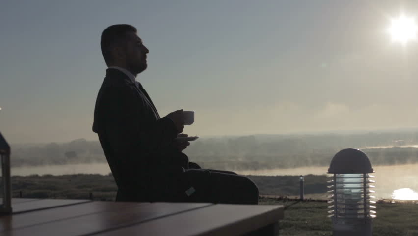 Portrait of a young businessman drinking coffee while sitting outdoors in a terrace table morning