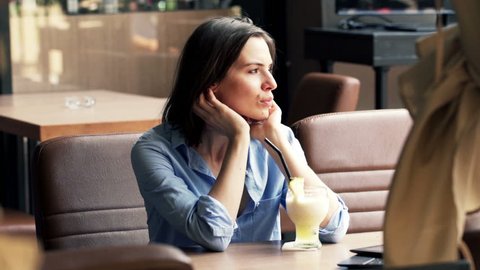 Unhappy, sad woman drinking cocktail sitting in cafe in city
