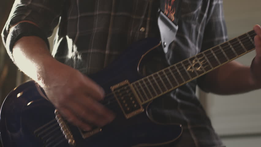 Handheld slow-motion A rock musician wearing a baseball cap plays guitar.