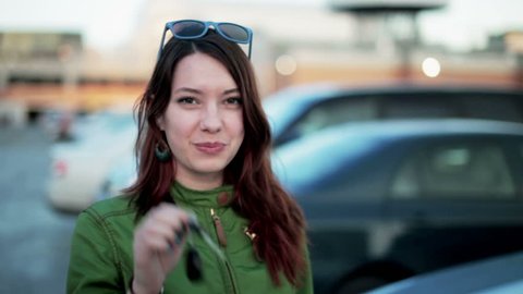 Young woman holding keys to new car auto and smiling at camera