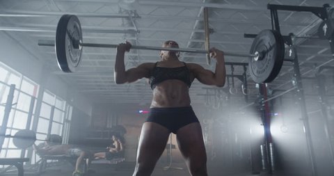 Medium shot slow mo tilt-down tilt-up men and women exercising and lifting weights female bodybuilder champion athlete doing power clean in cross fit gym