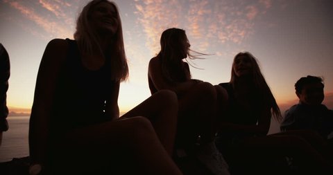 Smiling teens chatting while sitting on some rocks on a mountain together at dusk, Panning in Slow Motion Vídeo Stock