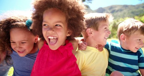 Happy mixed racial group of friendly children sitting in the sun laughing together, Panning in Slow Motion