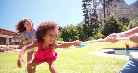 Little Afro girl having fun playing tug'o'war with friends in the garden in Slow Motion