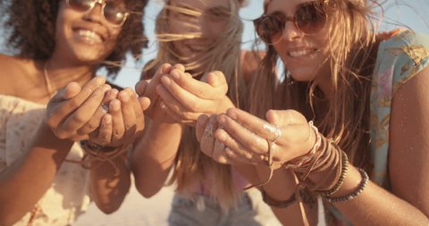 Mixed race group of girls blowing colorful confetti from their hands happily on a beach at sunset in Slow Motion