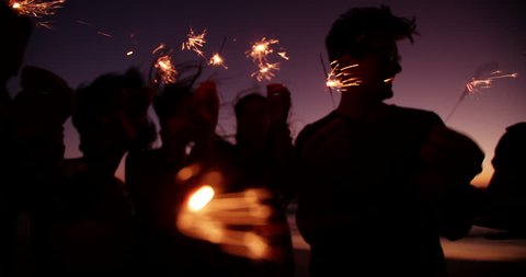 Group of friends having a beachparty together and celebrating with sparklers in the twilight in Slow Motion