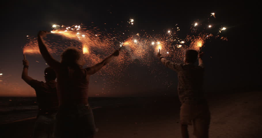 Rearview of friends running together on a beach holding sparkling fireworks in Slow Motion