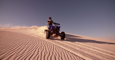 Competitive quad bike racer kicking up sand and dust while travelling up a sand dune, Panning in Slow Motion