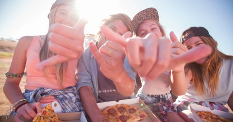 Portrait shot of a group of teen friends sitting together outdoors eating pizza with sun flare, Panning in Slow Motion