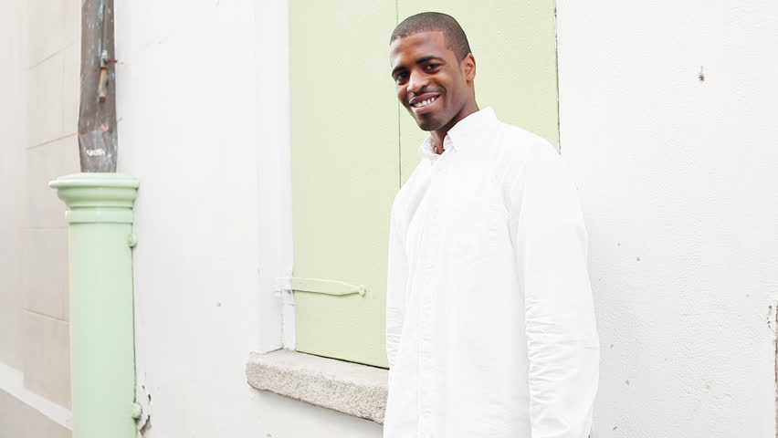 Black man smiles at the camera and plays a trumpet in the street