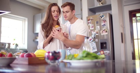 Cheeky boyfriend stealing a bite of his girlfriend's muffin in the kitchen early in the morning in Slow Motion