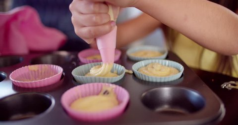 Cropped shot of a mom and daughter in the kitchen squeezing cupcake dough into cupcake holders in a baking tray, Slow Motion