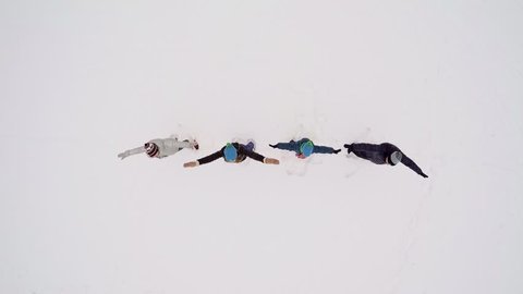 Four people family fall down on snow and wave hands at winter day. Aerial view