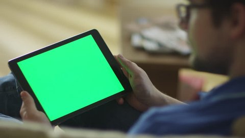 Man is Laying on Couch at Home and Using Tablet with Green Screen in Landscape Mode. Shot on RED Cinema Camera in 4K (UHD).