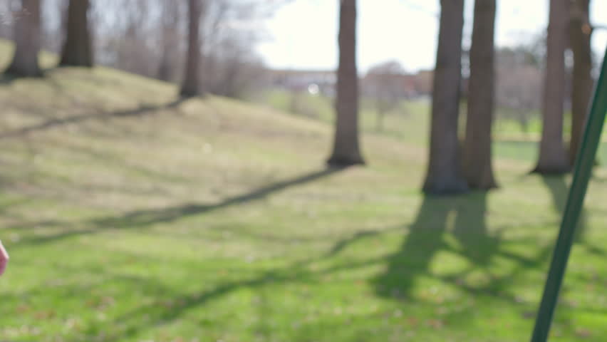Side, rear view of playground swings with boy being pushed by mom as he goes in and out of shot.  Park playground on warm spring day.  Close view, focus on boy.  Recorded in slow motion 4K at 60fps