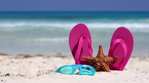 Pink flip flops, swimming glasses and starfish on white sandy beach. Summer vacation concept
