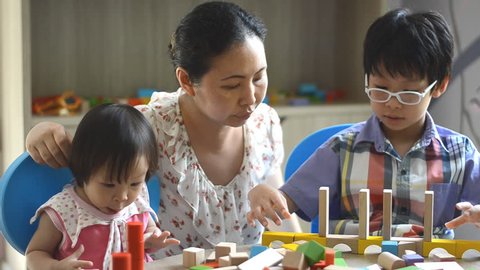 Little asian children and mother playing with colorful construction blocks on table  Adlı Stok Video