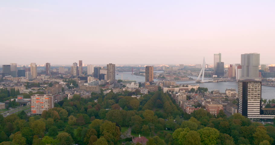 Pan tilt right aerial view motion video of Rotterdam city skyline with modern Erasmusbrug bridge, dutch skyscrapers architecture of downtown and sunset sky, South Holland, Netherlands, Europe