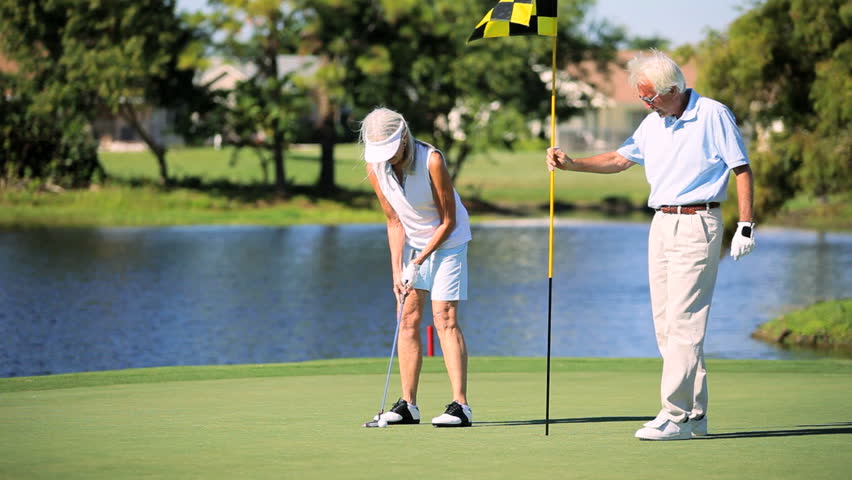 Senior lady sinking her golf putt while her husband celebrates
