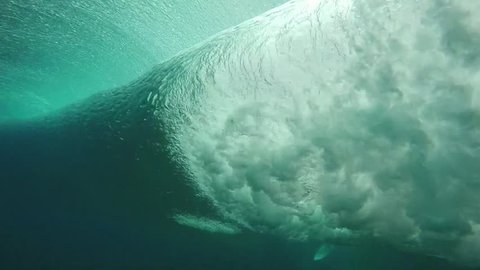 Underwater view of surfer trying to dive under wave breaking over coral reef, slow motion