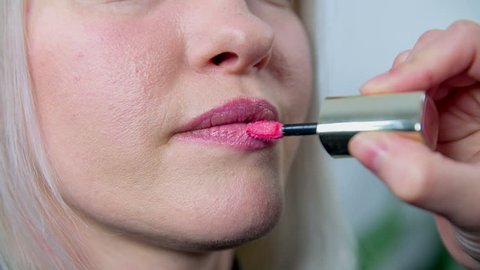 Putting on the lipstick . Slow motion close up RAW footage of a woman getting her lips done by a young beautician with pink lipstick.