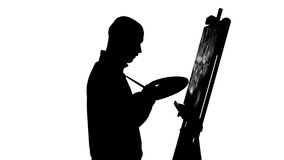 Talanted, bald, stylish, bearded painter in dark sweater continues drawing a painting  by oil paints holding the palette in his hand on white background, silhouette