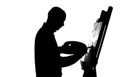 Talanted, bald, stylish, bearded painter in dark sweater continues drawing a painting  by oil paints holding the palette in his hand on white background, silhouette, slow motion