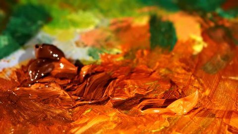 Painter mix brown and orange colors oil painting on palette with other different and colored paints like green brown, yellow, close up