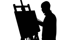 Bald, stylish, bearded painter in dark sweater drawing a painting  by oil paints holding the palette in his hand on white background, silhouette, slow motion