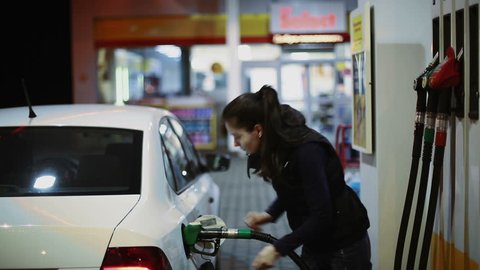 Woman refueling car at gas station pump at night