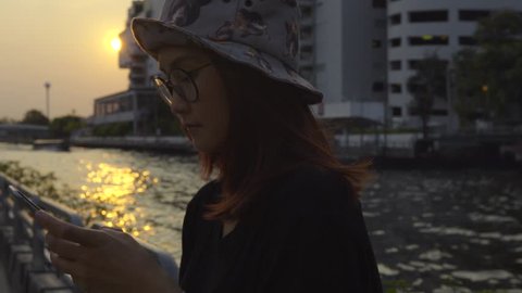 beautiful woman texting on smartphone in the city waiting for a boat,sunset time