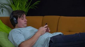 Man playing games on the phone. Slow motion total RAW footage of a man lying o the couch and listening to the music and playing games on the smart phone.