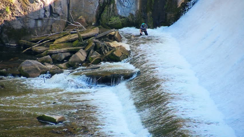 The big dam on the river. Fishing in rough river under the waterfall. Fishermen on the stones catch fish in the rough water of special mesh. The sequence