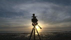 Video camera set up on tripod filming time lapse of sunset over the Pacific Ocean in Oregon.