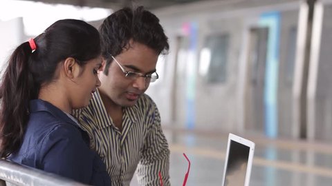 Young office going Indian man and woman working on lap top on metro station.