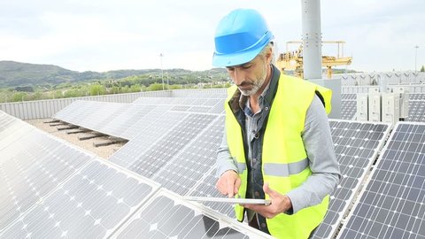 Mature engineer on building roof checking solar panels