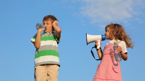 girl laughing through megaphone, boy drinking water and plugging up ear