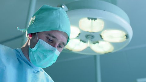 Closeup shot of male surgeon performing an operation. His assistant wipes sweat drops from his forehead using gauze pad.