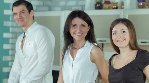 Three friends are preparing themselves healthy dinner and smiling directly at the camera. Young smiling friends cook dinner in kitchen while cut vegetables. Food cooking together.