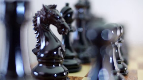Chess Board and Pieces. Black lacquered pieces with defocused glare from lighting. Closeup. Shallow depth of field. Dolly shot. Follow focus