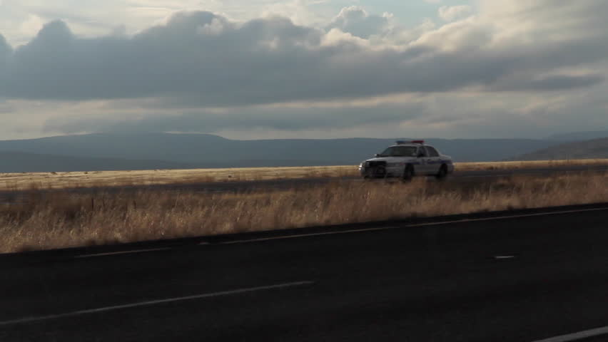 Police Car driving alone down highway while the sun is setting 
