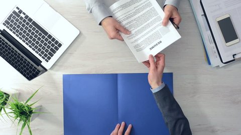 Businessman checking a candidate's resume during a job interview and shaking hands after hiring him, hands top view