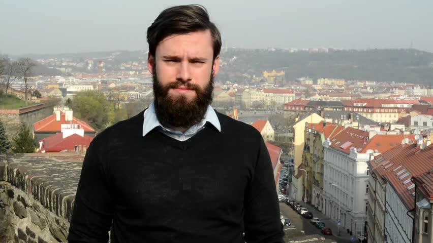 young handsome man with full-beard (hipster) talks to camera and agrees - city in background 