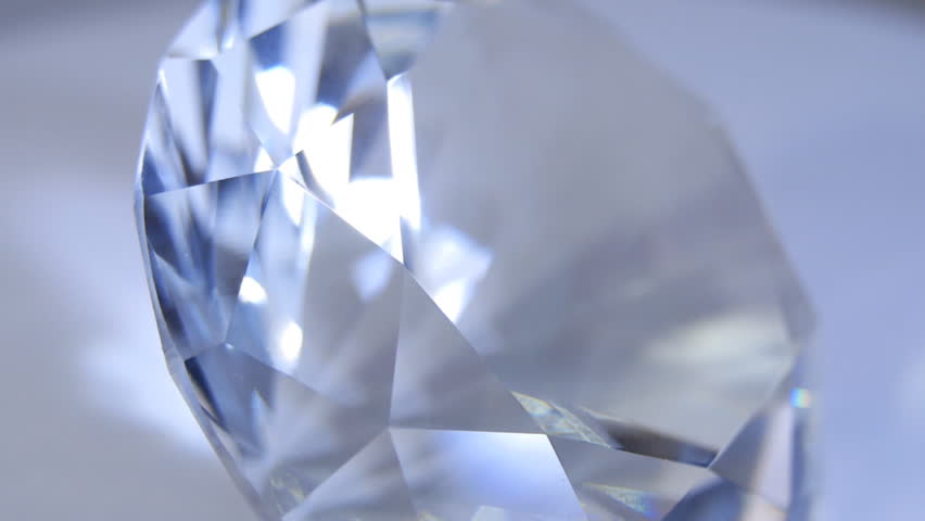 Facets of a diamond sparkle the bright light. Diamond rotating on light background. Extreme closeup. Shallow depth of field. Dolly shot
