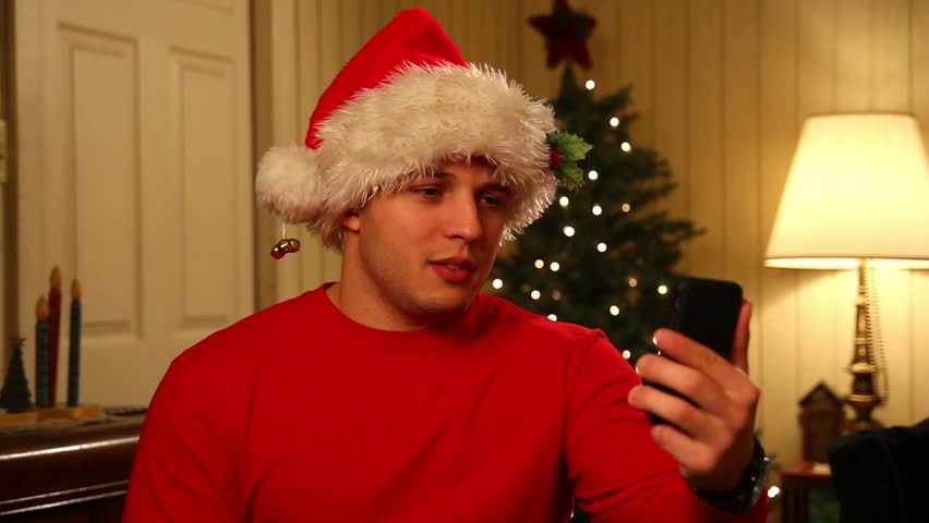 A young man in a Santa hat video chats on his mobile smartphone.
