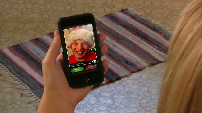 Male in Santa hat video chatting on a generic, portable handheld device.  Screen