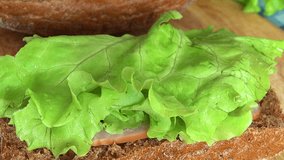 Close-up View of Man Making a Delicious Sandwich of Rye Bread with Tomatoes, Cucumber, Lettuce, Sturgeon, Cheese and Spices on a table. Full HD 1920x1080 Video Clip